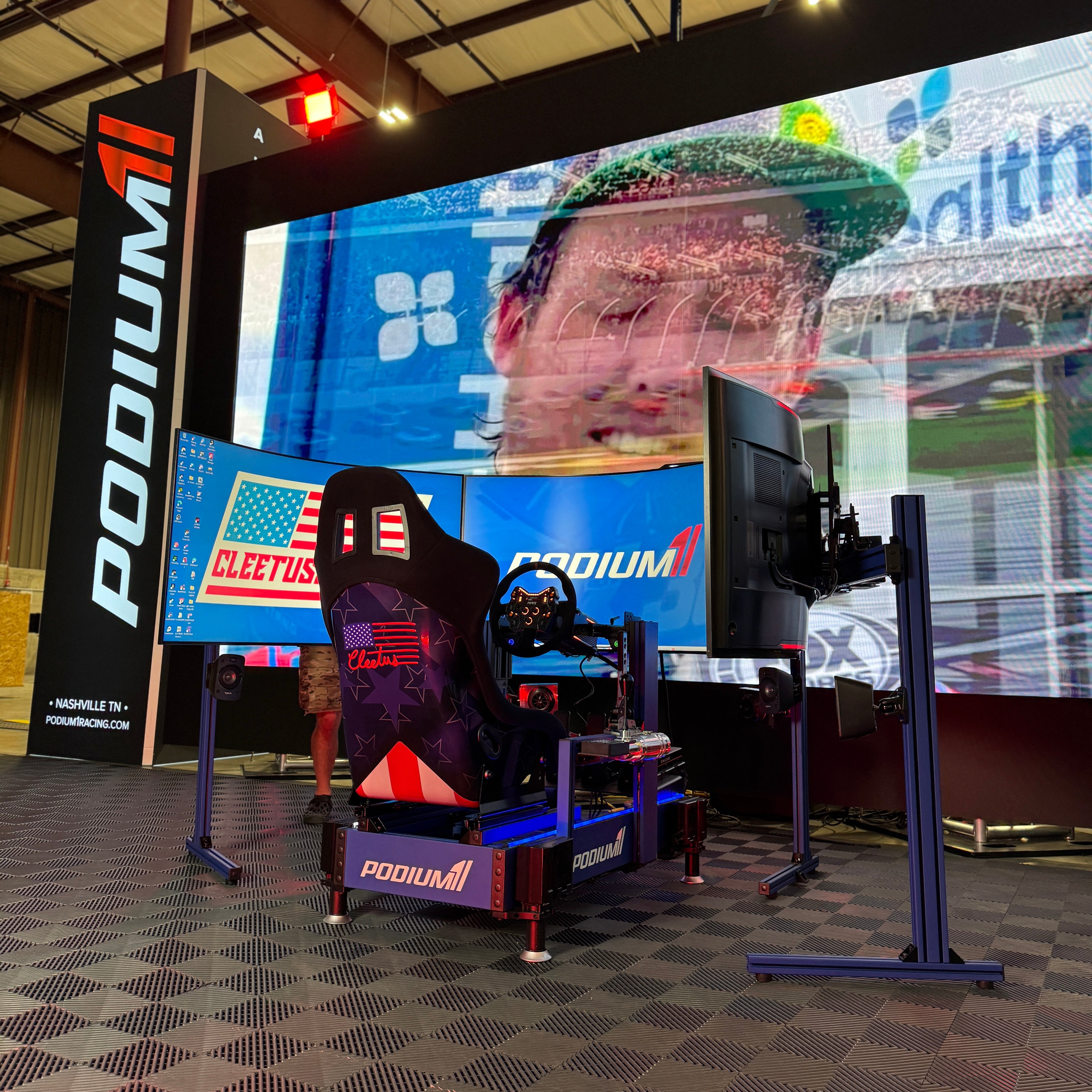 Simulator setup with a large screen displaying a person, branded with 'PODIUM' and 'Cleetus'.